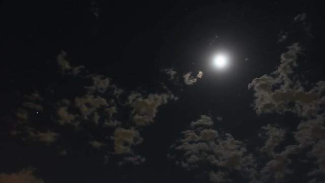 Timelapse of clouds moving across the sky under moon at night time with some stars visible in the backgound.
