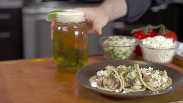 Tracking shot of tacos with foamy beer set down on chopping block
