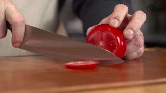 Dolly shot of chef slicing ripe red tomato with kitchen knife