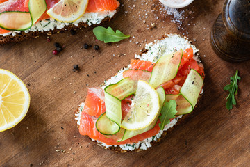 Sandwich with salmon, cucumber and cream cheese on wooden background, top view. Healthy salmon...