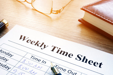 Weekly time sheet and pen on an office desk.