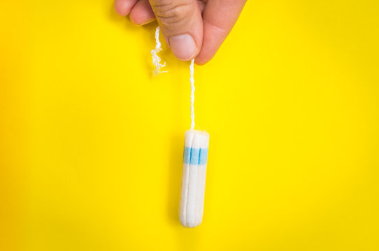Woman is holding menstruation tampon in hand on yellow