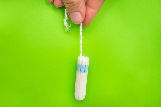 Woman is holding menstruation tampon in hand on green