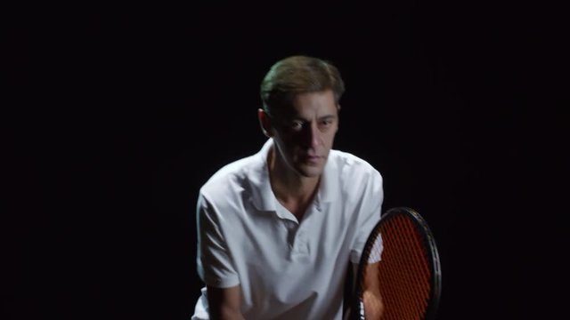 Studio shot of mature male tennis player with racquet standing in ready position isolated on black background