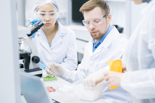 Portrait of three scientists doing research studying substances in modern laboratory, focus on young man wearing protective glasses