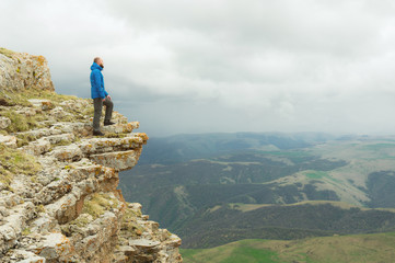 bearded hipster tourist man standing on the edge of a rock and looking out into the distance on an epic plateau. The concept of tourism