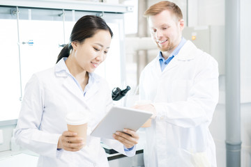 Waist up portrait of two modern young scientists wearing lab coats taking break from working in...