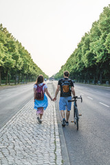 Obraz premium rear view of couple with backpacks and bicycle walking at street