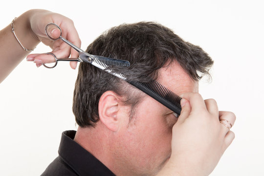 Hairdresser cutting handsome young man having haircut with scissors in studio
