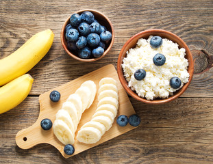 Brown wooden Bowl of homemade curd with banana, jam, blueberries on a dark brown wooden background, top view, copy space