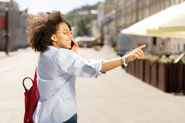 One second please. Cheerful young woman making a phone call while asking someone across the street to wait for her