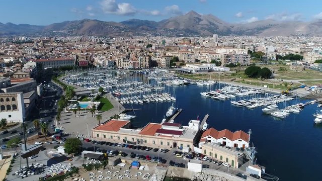 Aerial footage of marina yacht club located at Palermo Sicily Italy showing streets on left and harbor on right furthermore showing the city center and mountains in background 4k high resolution
