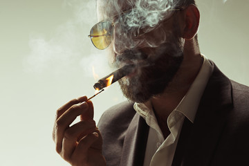 The barded man in a suit holding cigar - obrazy, fototapety, plakaty