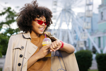 Long expectation. Pleasant curly-haired woman waiting for her friend and looking at a watch with a...