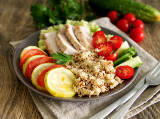 Healthy vegetable buddha bowl lunch with turkey, vegetables and quinoa on brown wooden background. Side view.
