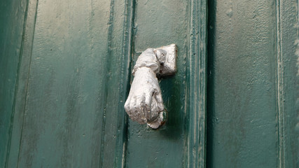 A silver door knocker in the shape of a hand, against a green wooden door