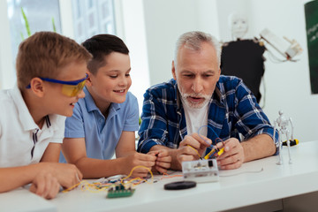 Smart grandfather. Positive joyful man talking to his grandchildren while explaining to them how to build a robot