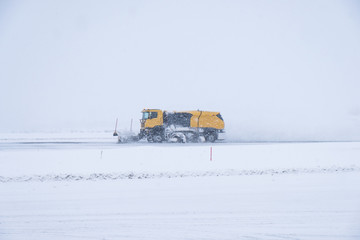 Yellow snow ploughs plowing snow cover road in blizzard