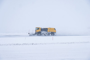 Yellow snow ploughs plowing snow cover road in blizzard