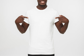Smiling nice african american man pointing at blank white t-shirt with both index fingers, copy...