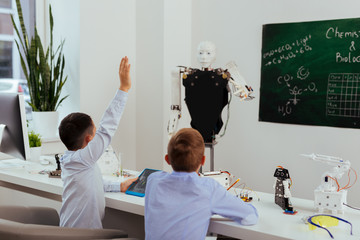 Smart pupil. Nice smart boy holding his hand up while knowing the answer to the question