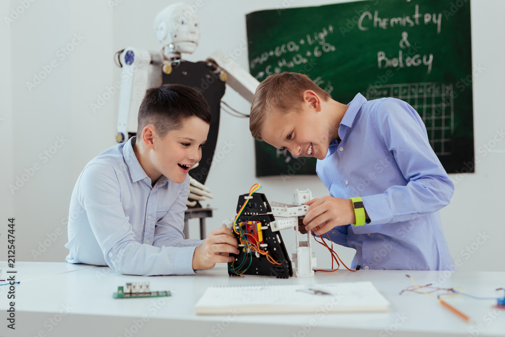 Wall mural modern classroom. nice cheerful boys looking at the robot while playing in the classroom