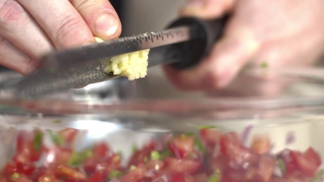 Close-up tracking shot of chef grating fresh garlic clove over bowl of salsa