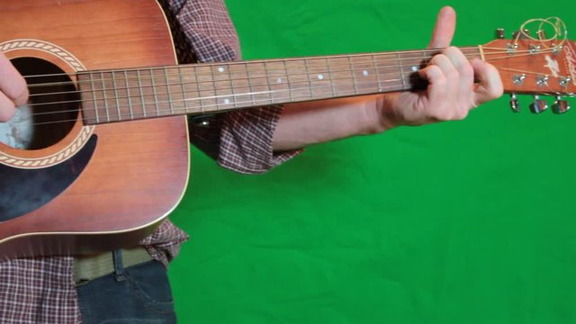 Close up sliding, dolly shot of a man playing a guitar with a green screen in the background.