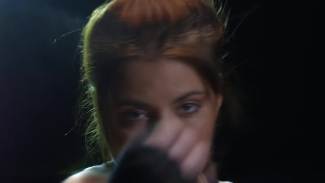 Studio shot of strong female fighter with hand wraps looking at camera and shadowboxing against black background