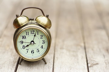 Analog alarm clock on wooden table with blur green garden background, 8 am., copy space