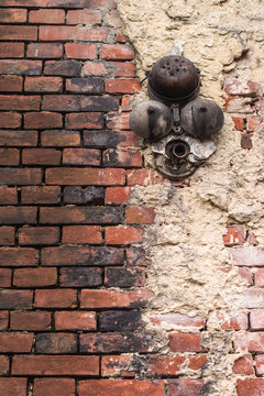 An old battered brick red wall with white plaster and a rusty broken bell © okrip