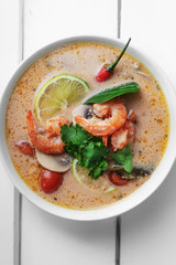 Traditional thai soup tom yum with shrimps and mushrooms, served with fresh lime slices. Close up shot, white rustic wooden background.