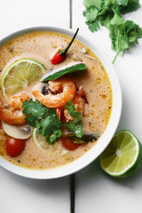 Traditional thai soup tom yum with shrimps and mushrooms, served with fresh lime slices. White rustic wooden background.
