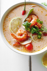 Traditional thai soup tom yum with shrimps and mushrooms, served with fresh lime slices. Close up shot, white rustic wooden background.