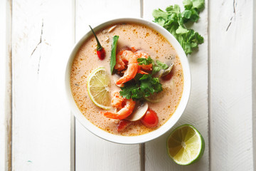 Traditional thai soup tom yum with shrimps and mushrooms, served with fresh lime slices. White rustic wooden background.
