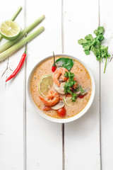 Traditional thai soup tom yum with shrimps and mushrooms, served with fresh lime slices. White rustic wooden background.