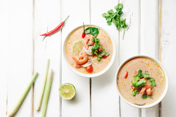 Traditional thai soup tom yum with shrimps and mushrooms, served with fresh lime slices. White rustic wooden background.