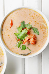 Traditional thai soup tom yum with shrimps and mushrooms, served with fresh lime slices. Close up shot, white rustic wooden background.