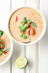 Traditional thai soup tom yum with shrimps and mushrooms, served with fresh lime slices. White rustic wooden background.