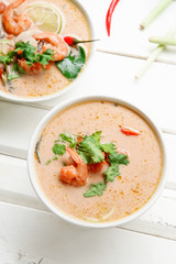 Traditional thai soup tom yum with shrimps and mushrooms, served with fresh lime slices. White rustic wooden background.