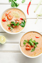 Traditional thai soup tom yum with shrimps and mushrooms, served with fresh lime slices. White rustic wooden background.