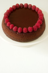 Chocolate brownie cake with raspberries and chocolate icing on a light background.