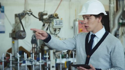 Young engineer in helmet works with table on the factory 4K