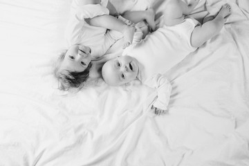 Two charming little babies lie on the white sheet and smile