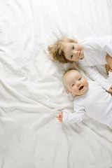 Two charming little babies lie on the white sheet and smile