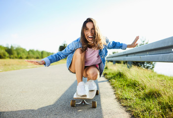Happy young woman riding longboard on  rural road © baranq