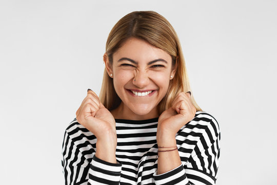 Lucky pretty girl with blonde hair reacting emotionally, biting lip and keeping fists clenched, showing excitement after she won in lottery. Success, achievement, joy, luck and celebration concept