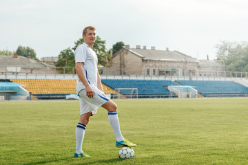 A football player stands on the field before the match and holds the ball with his foot. Determined to win the championship