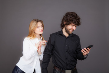 curious young woman over her shoulder peeking into the phone of a man. Photo taken in the studio