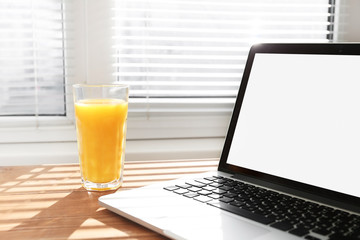 a glass of orange juice with a laptop on the window background
